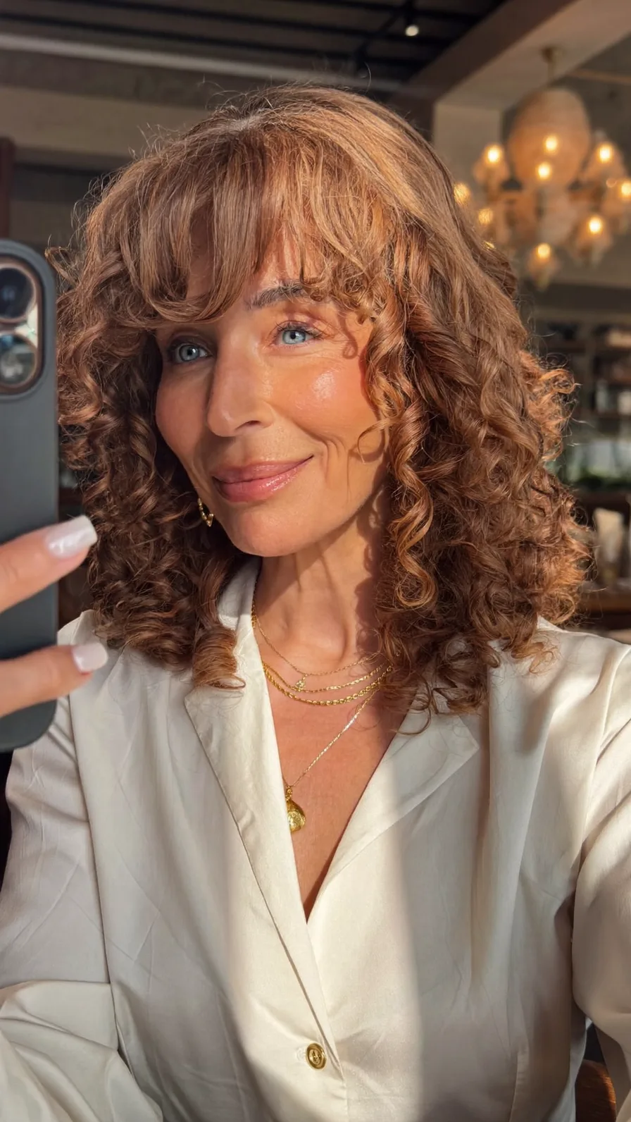 Voluminous Layered Curly Hair with Warm Highlights and Curtain Bangs
